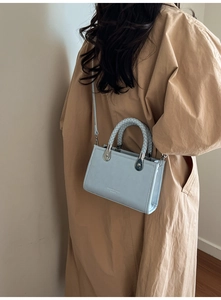 Detail of light blue crossbody bag with woven handle and elegant textured leather finish