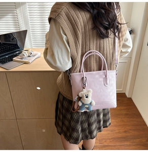 Detail showing light pink PU leather tote bag with long strap and cute white teddy bear charm