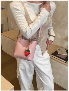 Dettaglio borsa a secchiello rosa con ciondolo a fragola e tracolla regolabile casual