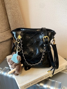 Chic black quilted bucket bag with gold chain and cute teddy bear charm on white book