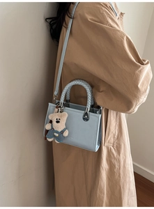Detail of light blue square handbag featuring woven ring handle and cute plush bear charm