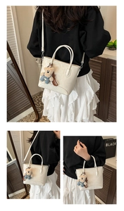 Detail of creamy white bucket bag featuring a cute teddy bear charm and sleek handles