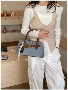 Détail du sac à main en denim bleu avec anses en cuir marron et pendentifs