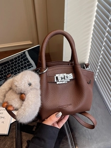 Brown leather pleated tote bag with silver lock and plush bunny charm on desk