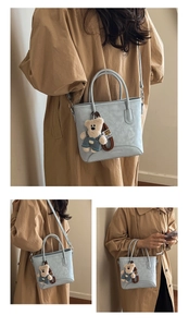 Detail view of light blue bucket bag featuring a teddy bear charm and textured finish
