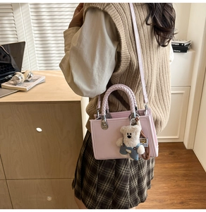 Pink crossbody bag with woven handle and cute bear charm shown in a lifestyle setting