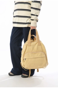 Detail of ginger yellow canvas backpack showing the top dual handles and zipper pocket