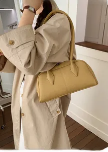 Minimalist ginger leather Boston bag shown on shoulder with stylish beige trench coat
