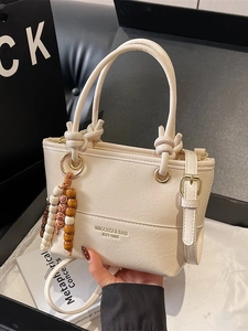 Chic beige crossbody handbag with top handles and decorative beaded charm accessory