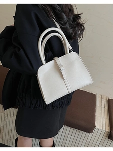 Détail d'un sac à main beige en similicuir texturé avec boucles argentées sur un manteau noir