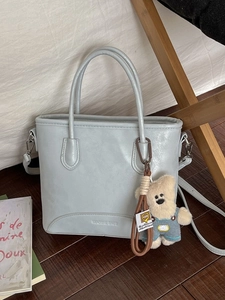 Light blue faux leather bucket bag with top handles and cute bear charm in soft lighting