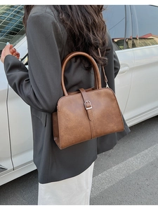 Sac à main vintage en cuir marron porté avec un blazer gris et un pantalon blanc