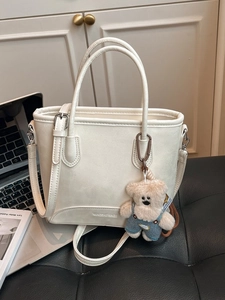 Elegant cream leather bucket bag with cute bear charm on a stylish black leather seat