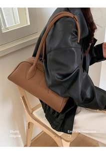Detail of a brown leather shoulder bag showing the texture and slender handle straps