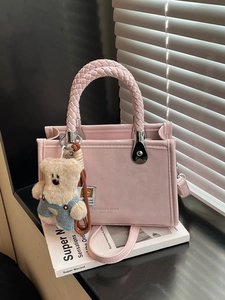 Pink fashion tote bag with woven handles and a cute bear keychain on a white book