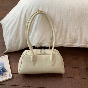 Macro detail of beige pebble leather pillow bag featuring dual metal zippers and wood floor