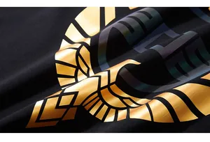 Close-up of golden geometric eagle print and iridescent lettering on black cotton t-shirt