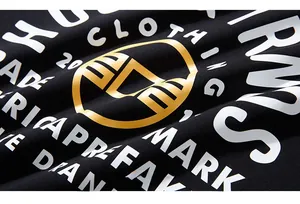 Makroaufnahme hochwertiger weißer und goldener Siebdruck-Buchstaben auf schwarzem T-Shirt