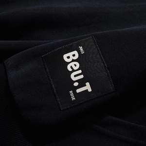Close-up of black hoodie sleeve with industrial woven label patch and Beu.T letter embroidery