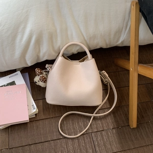 Detailed top view of a beige cloud bucket bag with a cute plush puppy charm on bed