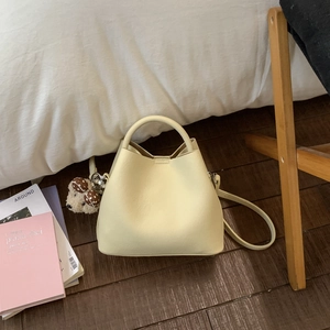 Detail view of cream bucket bag with plush bear charm on dark wood floor