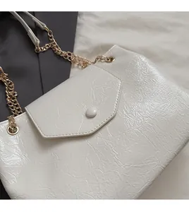 Détail de la texture en cuir plissé blanc et de la bandoulière chaîne dorée du sac