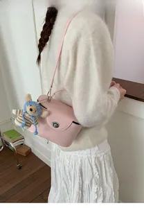 Pink matte leather crossbody bag featuring a metal twist lock and cute knitted bear charm