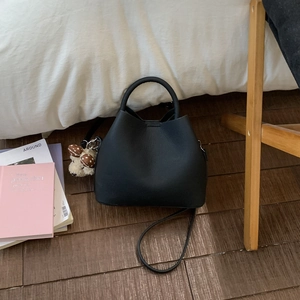 Detail of black matte leather bucket bag with a cute plush bear charm on a wood floor