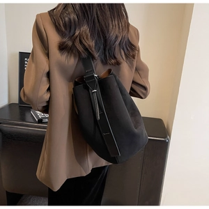 Detail of a matte black suede bucket bag with wide adjustable strap worn by a model
