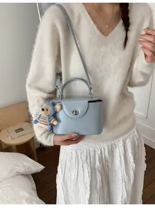 Detail of light blue box crossbody bag with silver lock and a cute teddy bear charm
