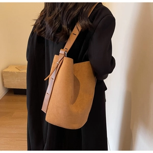Close-up of caramel brown suede bucket bag with adjustable leather strap worn by a model