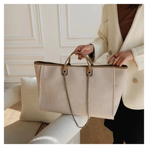 Detalle de bolso tote de lona crema con ribete marrón y elegante correa de cadena de plata