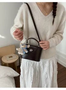 Detail of dark brown leather handbag with silver lock and a cute plush bear pendant