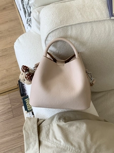 Elegant beige bucket bag with plush bear charm on white textured sofa background