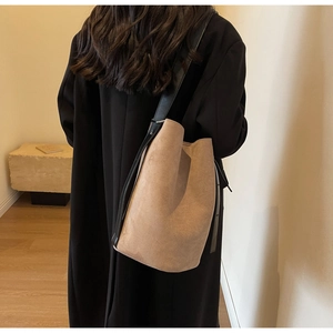 Close-up of khaki suede bucket bag with wide black leather strap on model shoulder