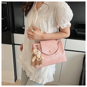Détail d'un sac à bandoulière rose clair avec chaîne dorée et breloque ours en peluche