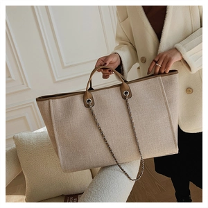 Detalle de bolso tote tejido beige con asas de cuero marrón y cadena sobre una modelo