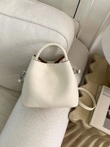 Chic cream white bucket bag with textured leather and silver hardware on a cozy sofa