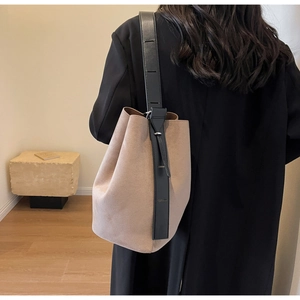 Detail of minimalist beige suede bucket bag with adjustable wide black shoulder strap on model