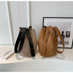 Detail of minimalist suede bucket bags in light grey and caramel with wide leather straps
