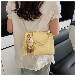 Sac à bandoulière jaune avec chaîne dorée et breloque ours porté par un mannequin