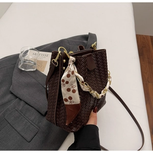 Détail du sac seau tressé marron foncé avec foulard cerise et poignée en chaîne