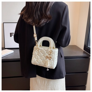 Detail of white quilted handbag with floral embroidery and pearl bow charm accessory