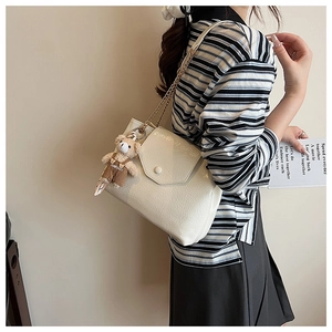 Détail du sac à bandoulière en cuir verni blanc cassé avec chaîne dorée et breloque ours