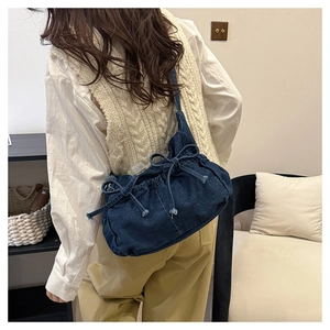 Detail of blue denim bucket bag featuring a decorative bow drawstring on a model