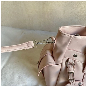 Close-up of silver metal buckle and rivet details on light pink PU leather handbag