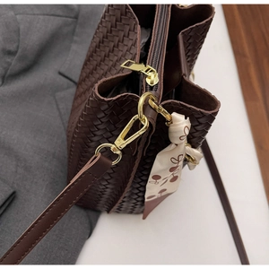Détail d'un sac à main tressé marron foncé avec ferrures dorées et foulard en soie floral