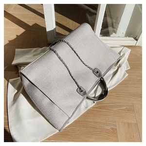 Detalle del bolso tote gris de lona con cadena metálica y asa de cuero elegante
