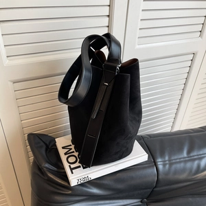 Retro black suede bucket bag with wide leather strap on sofa against minimalist background