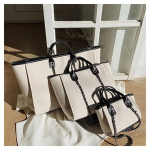 Tres tamaños de bolsos tipo cubo de lona beige con ribetes de cuero negro y cadena
